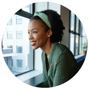 Profile of a smiling woman wearing a mint green headband and textured green outfit by a large window